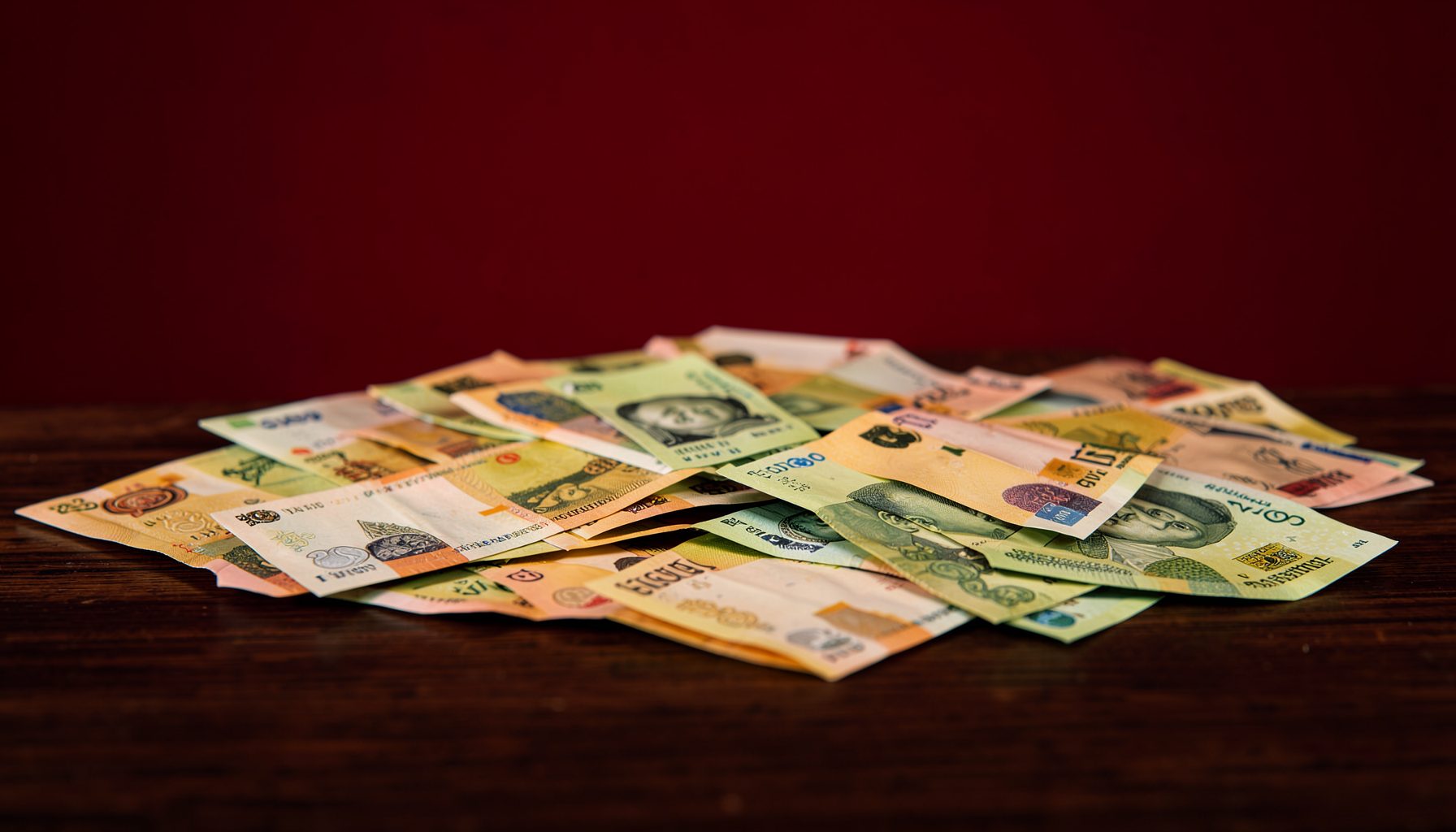 A close-up of Nigerian naira banknotes spread across a dark wooden desk, warm amber and green tones, crisp studio lighting.